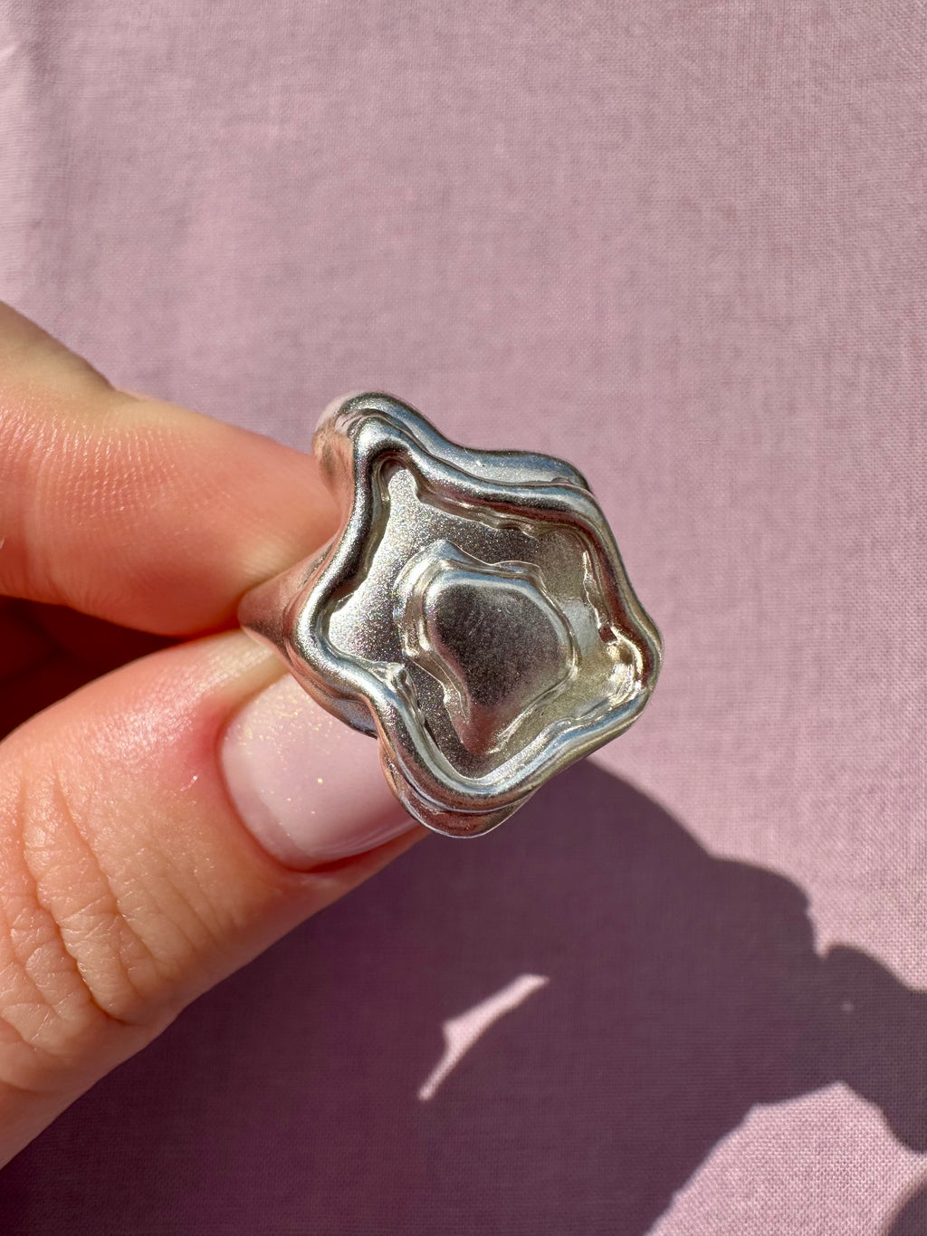 Silver ring held between fingers against a pink background