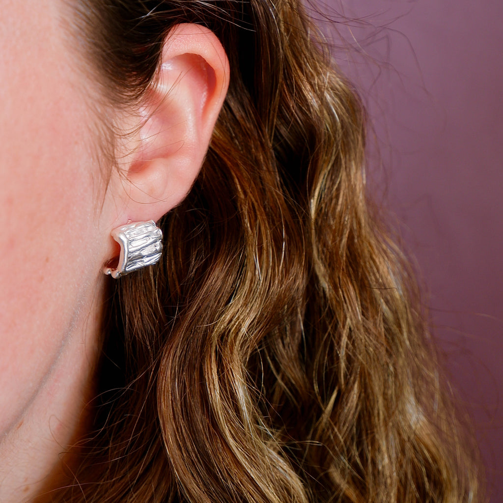 Close-up of an ear wearing a silver earring with wavy hair and a blurred background