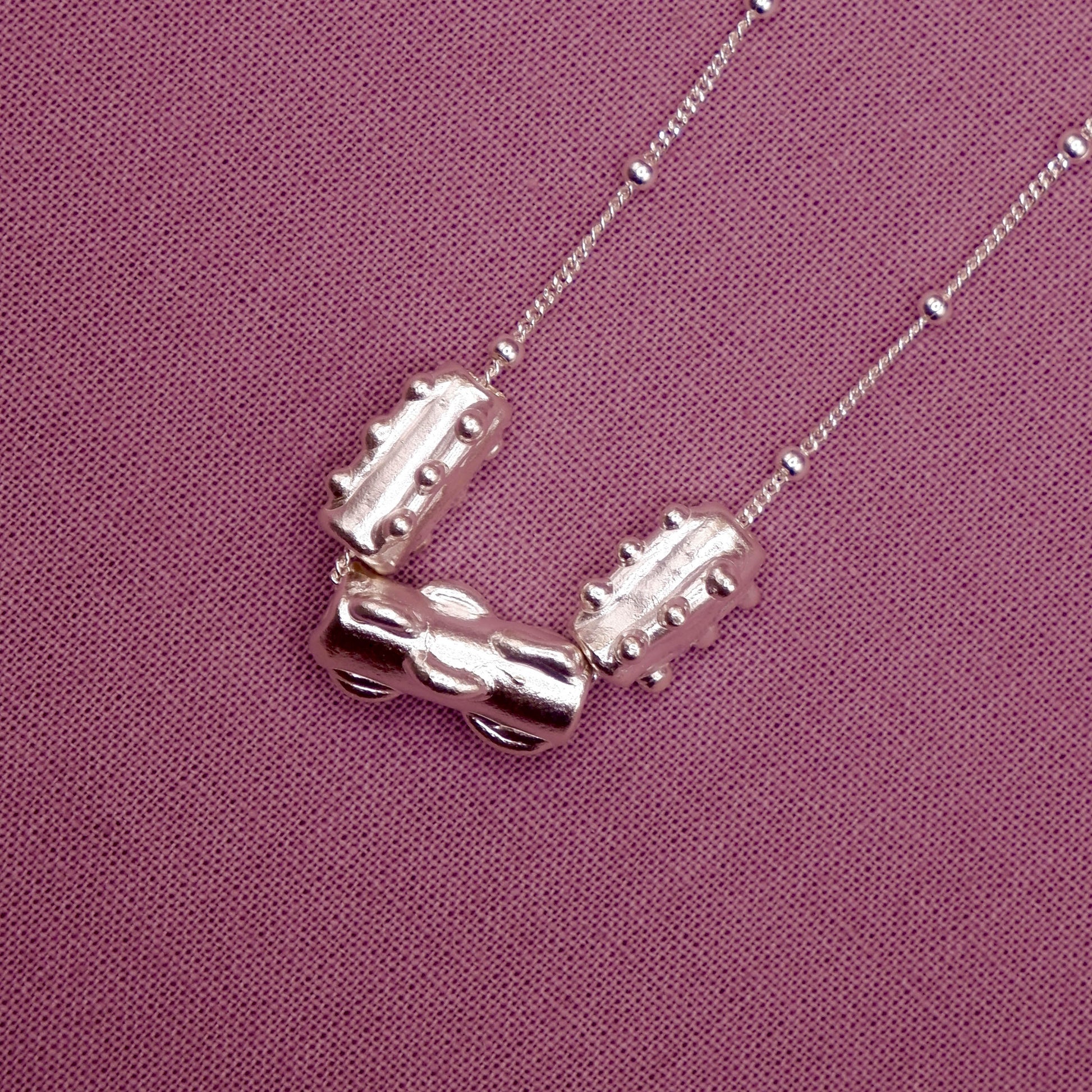 Silver necklace with three cylindrical beads on a purple fabric background