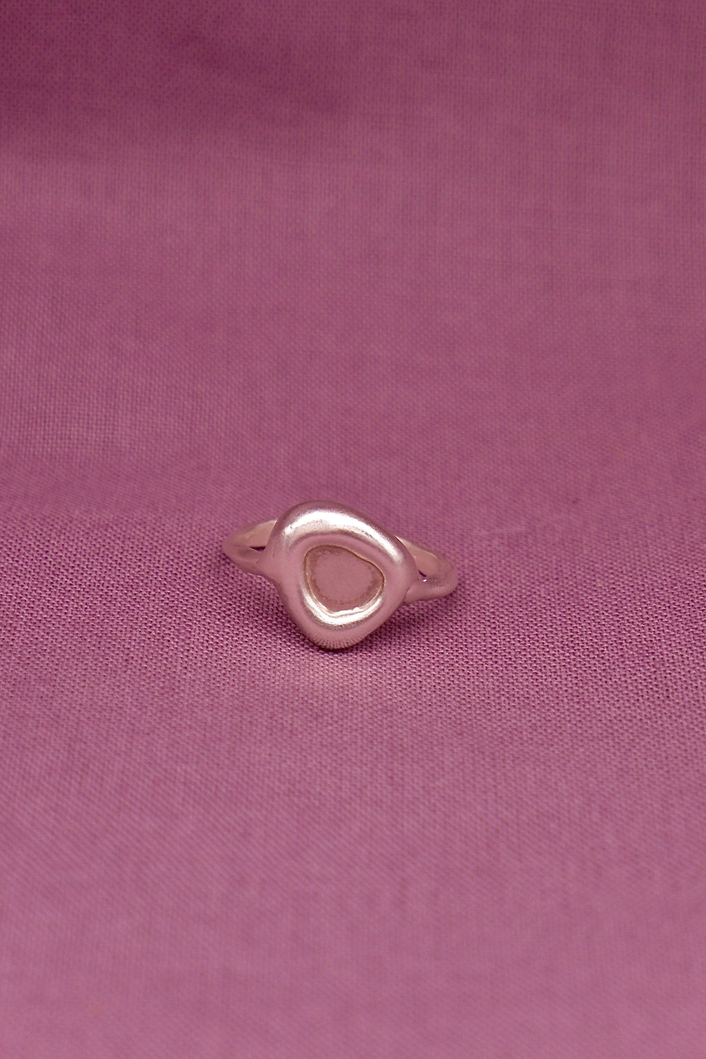 Silver ring with a triangle design on a pink fabric background