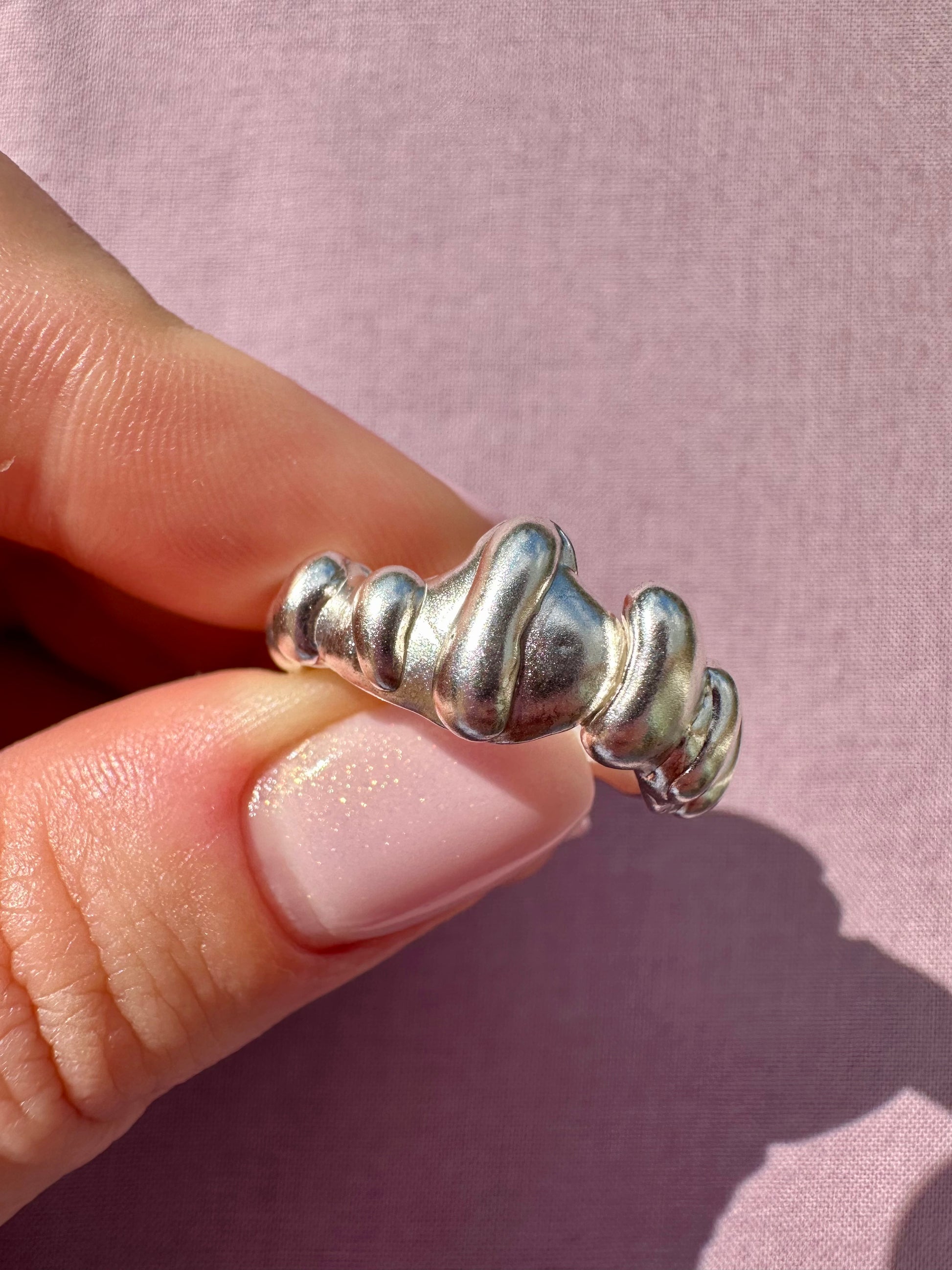 Silver ring with textured design held by a hand against a pink background