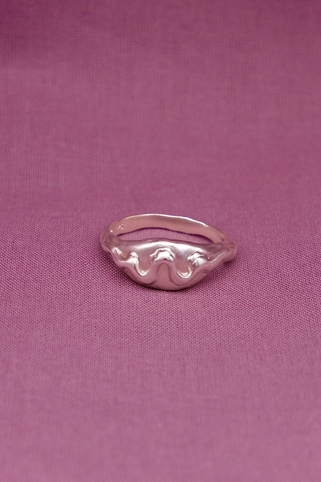 Silver ring with wavy design on a pink fabric background