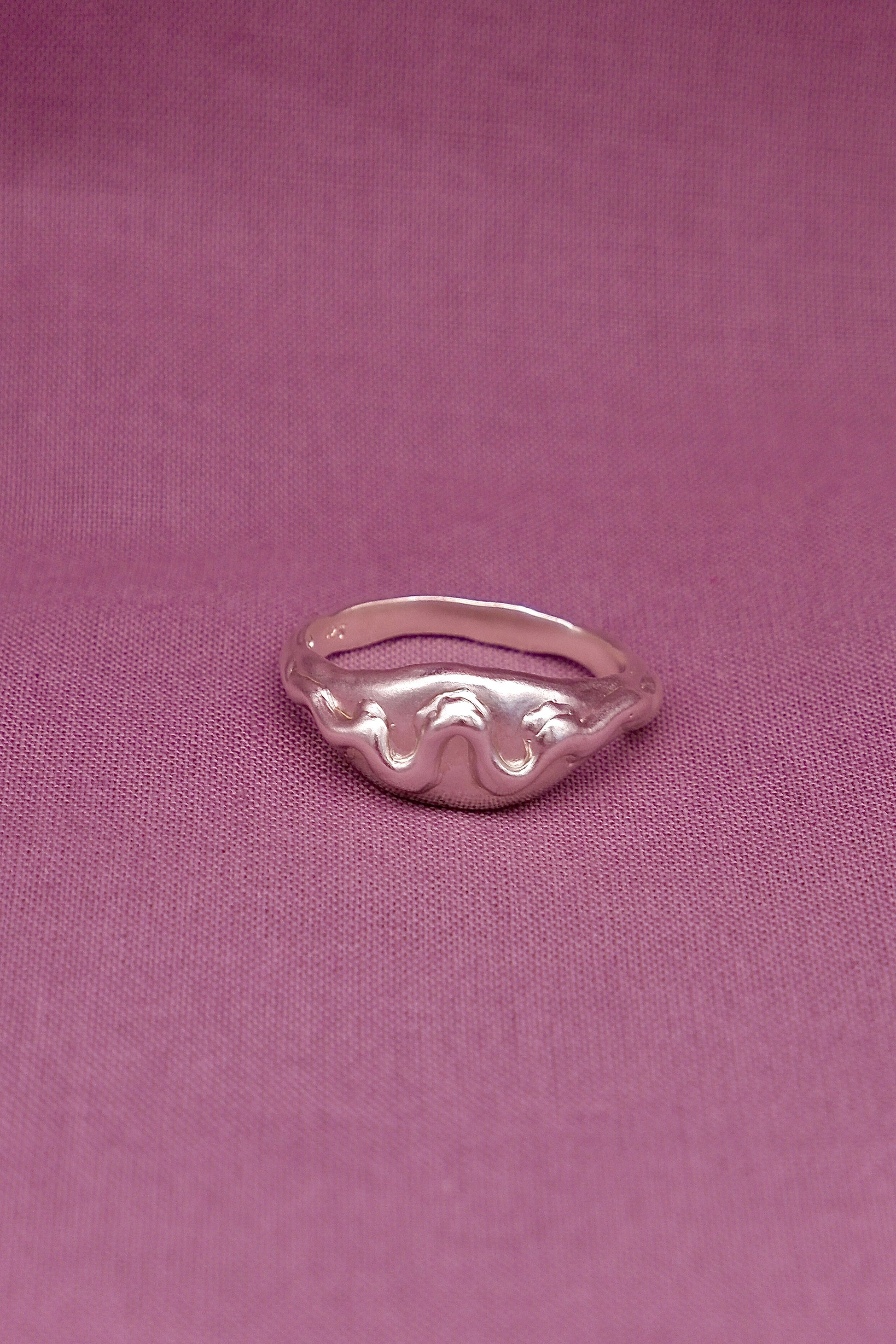 Silver ring with wavy design on a pink fabric background