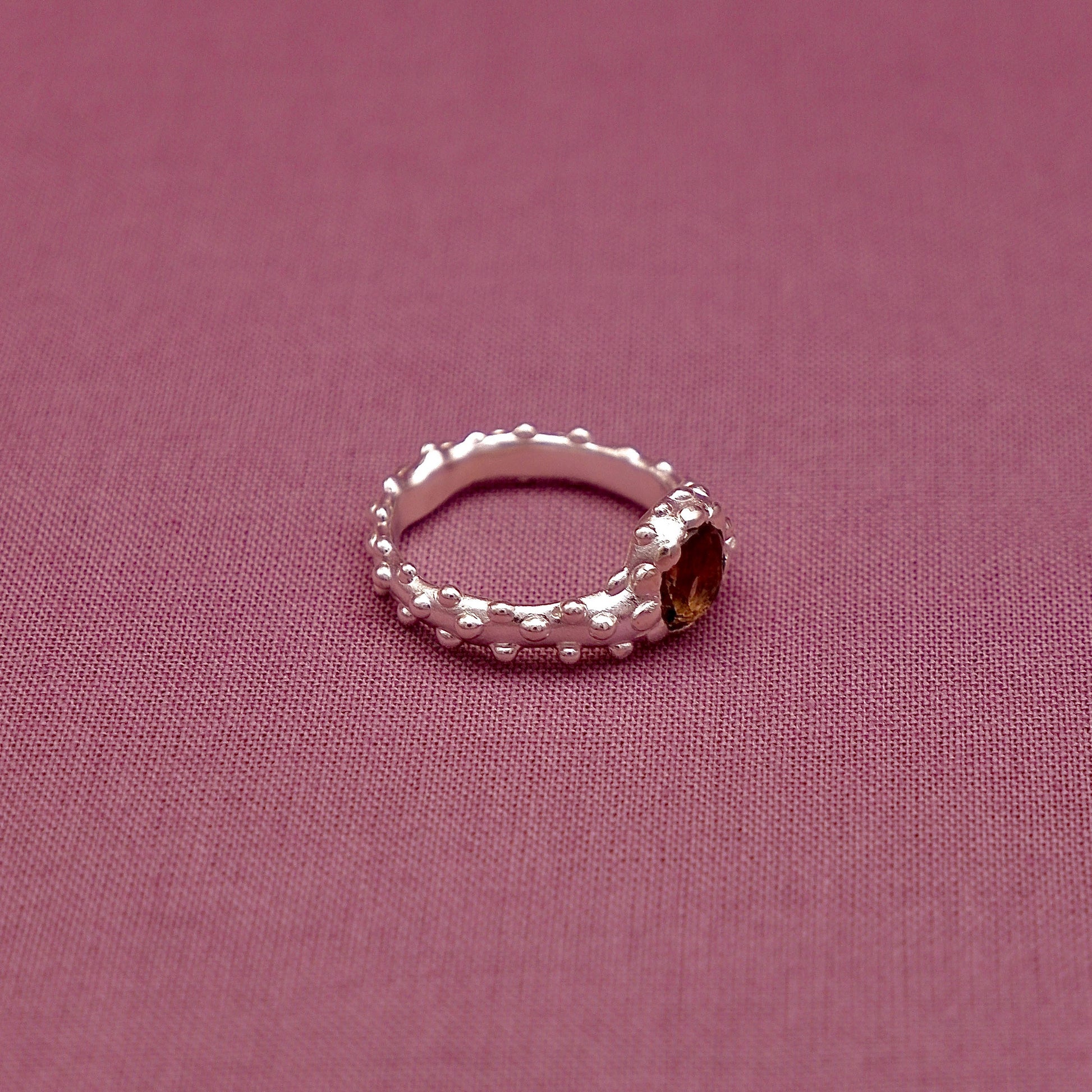 Silver ring with beaded design on a pink fabric background