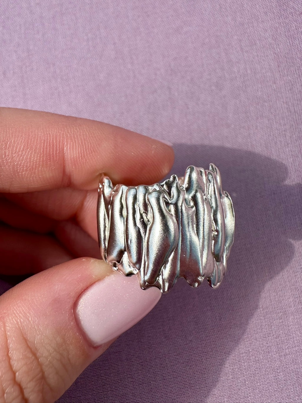 Silver ring held by a hand against a purple background