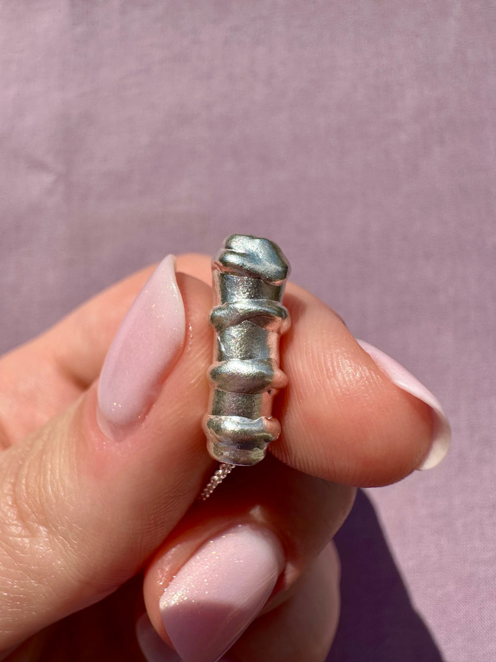 Silver bracelet with a textured design held between fingers against a light purple background