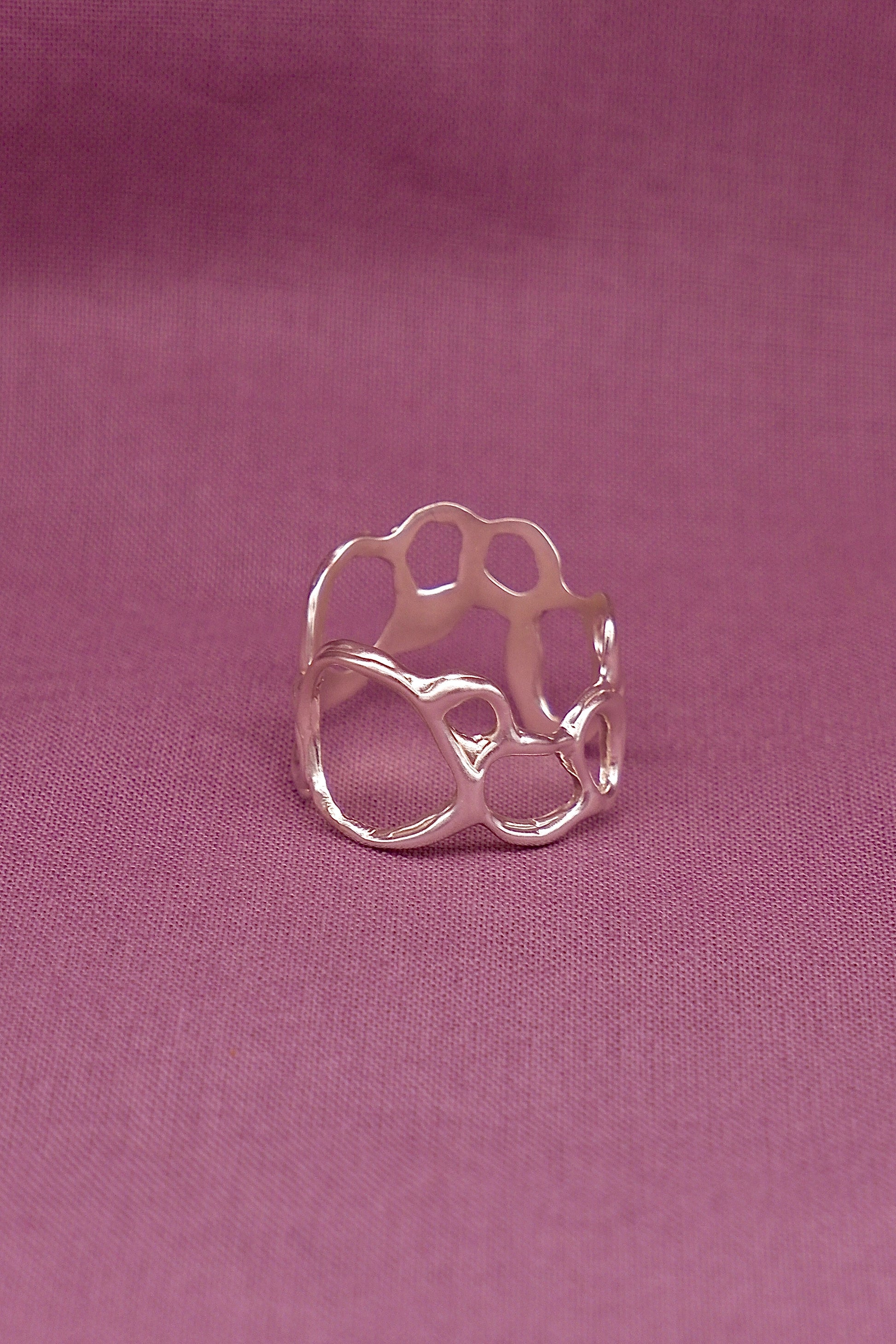 Silver ring with a textured design on a purple fabric background