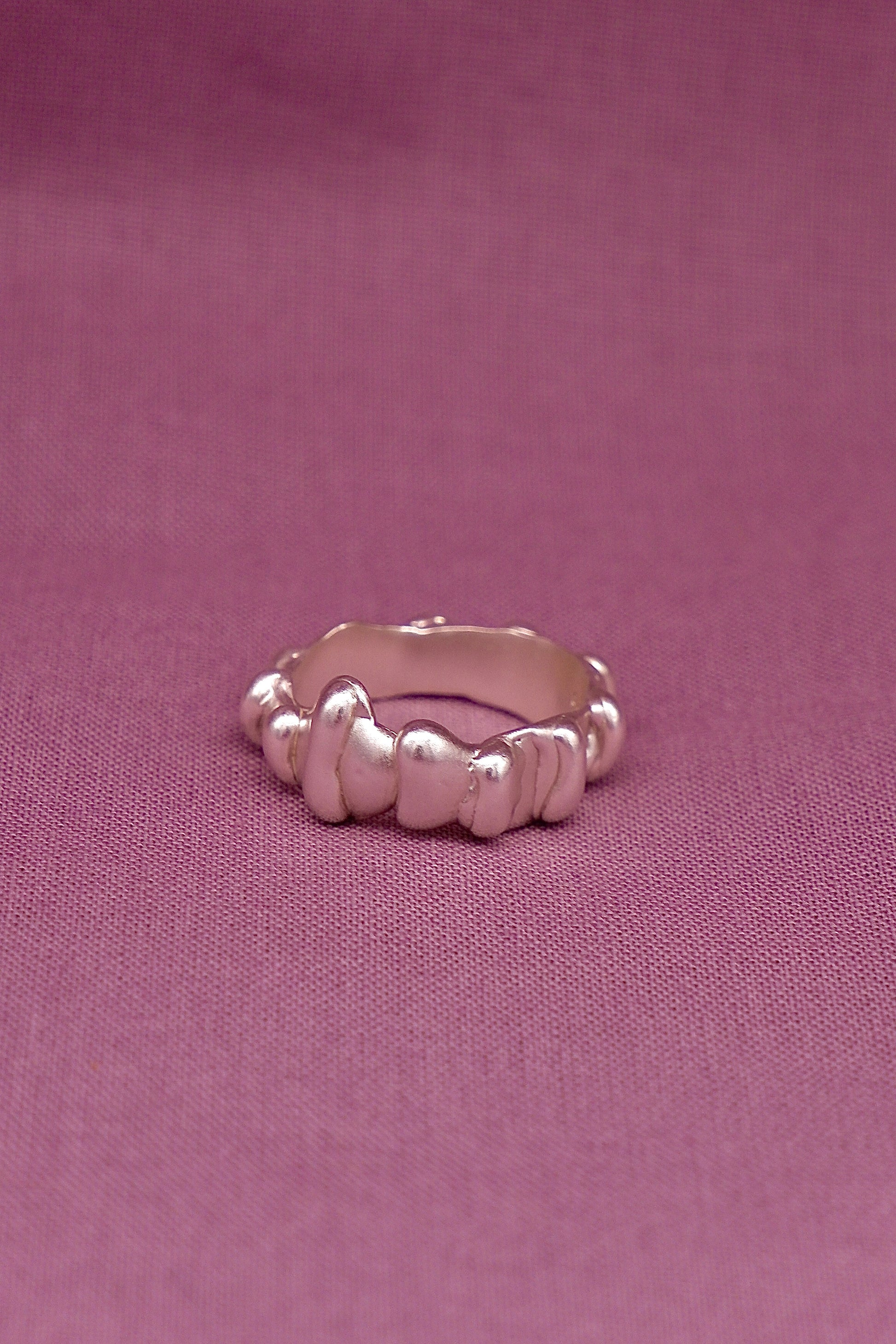 Silver ring with textured design on a pink fabric background