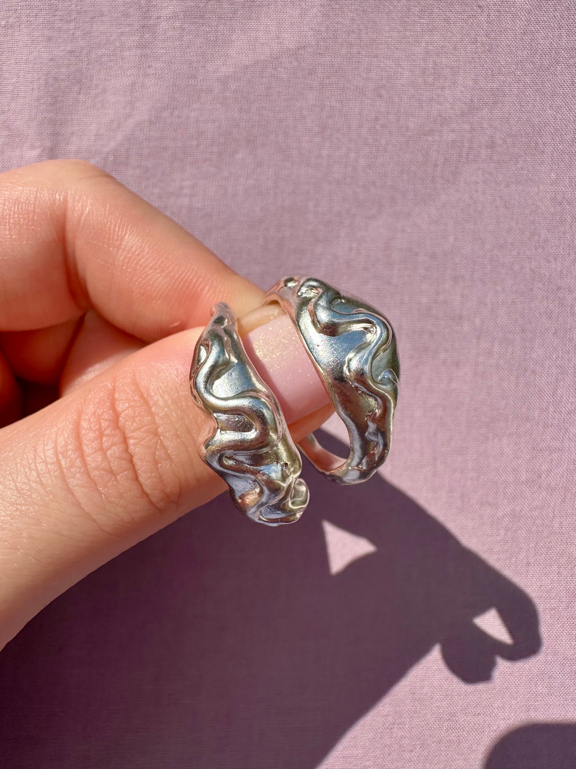 Silver rings being worn on fingers against a pink background