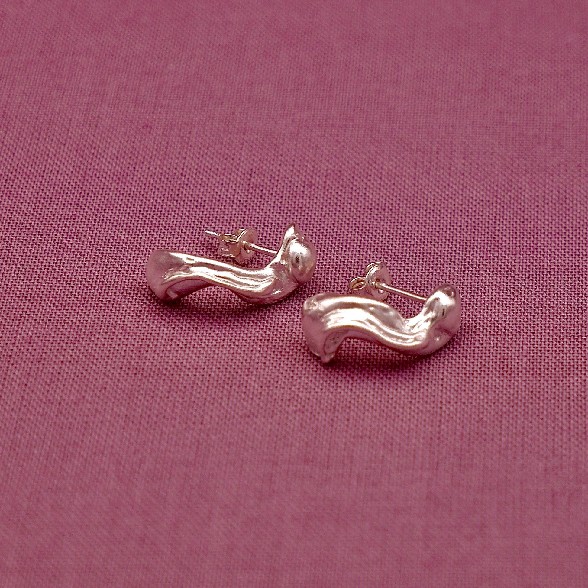 Silver earrings on a pink fabric background