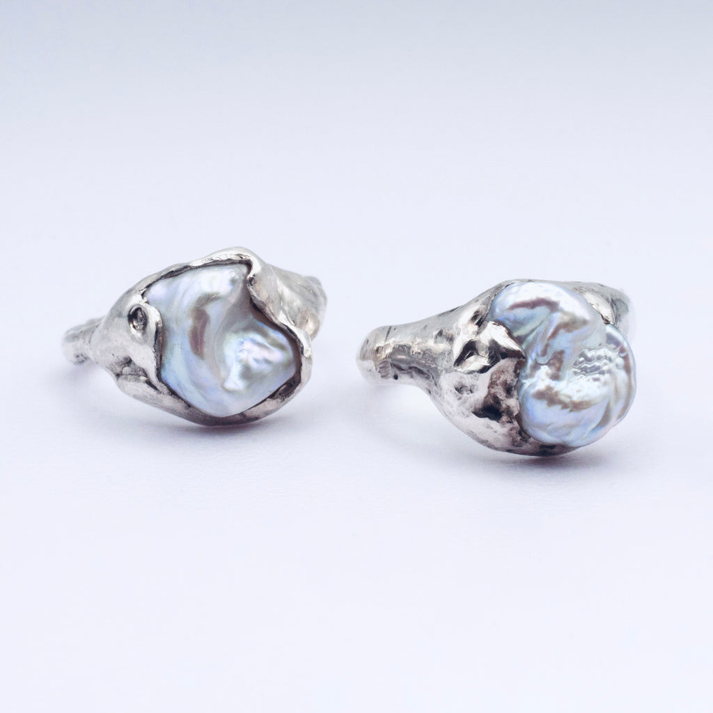 Pair of silver rings with large, irregularly shaped pearls on a white background