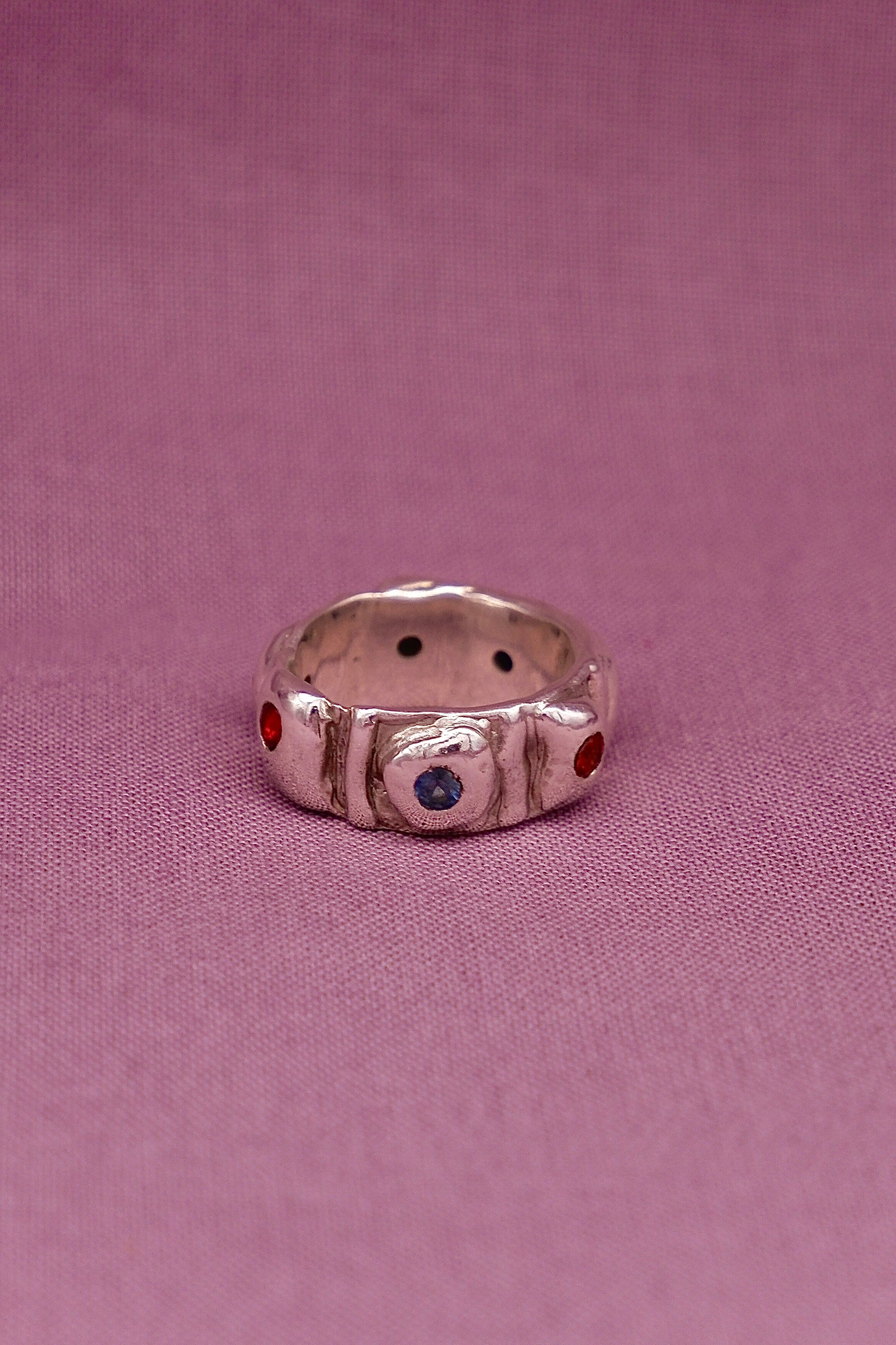 Silver ring with embedded gemstones on a pink fabric background