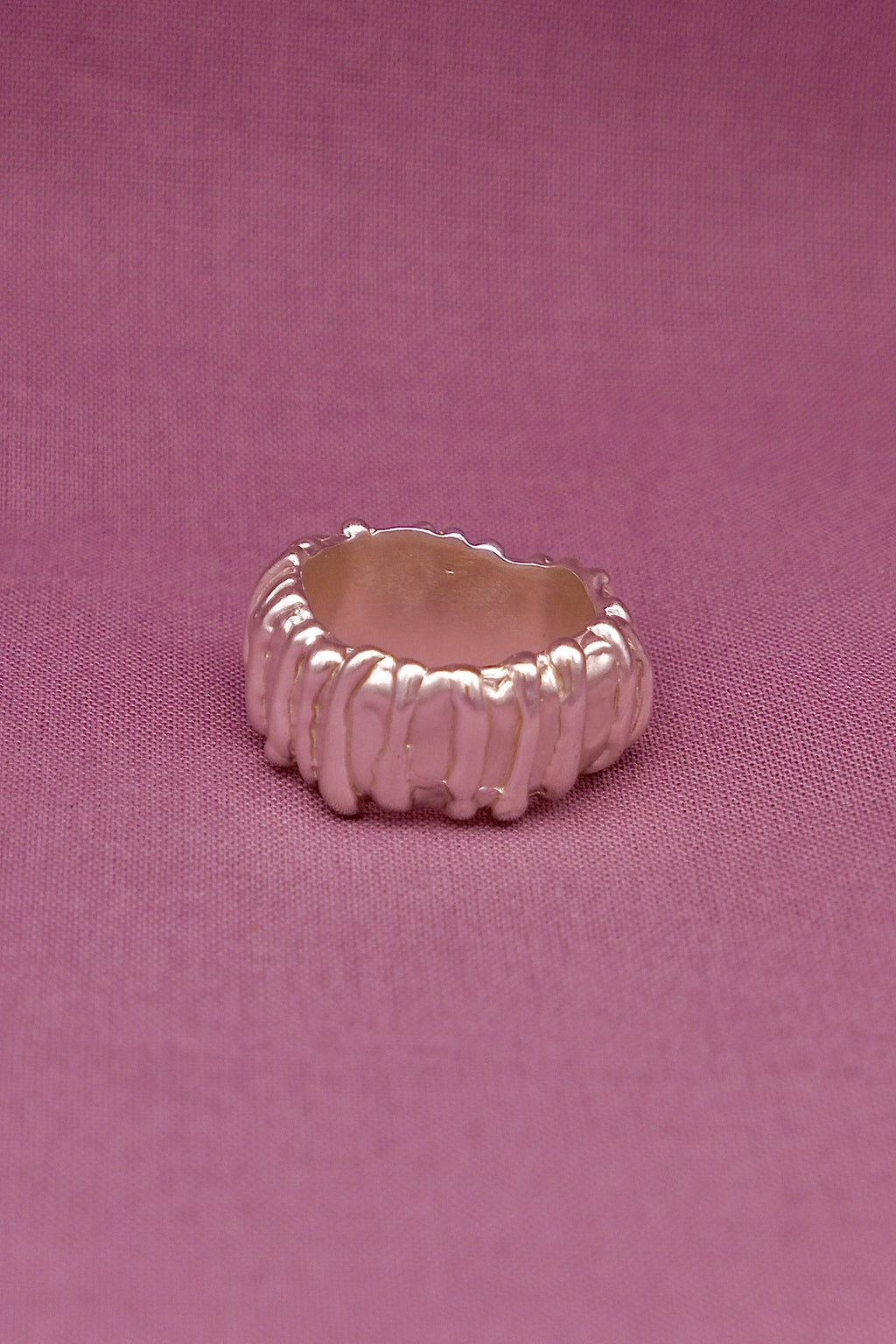 Silver ring with textured design on a pink background