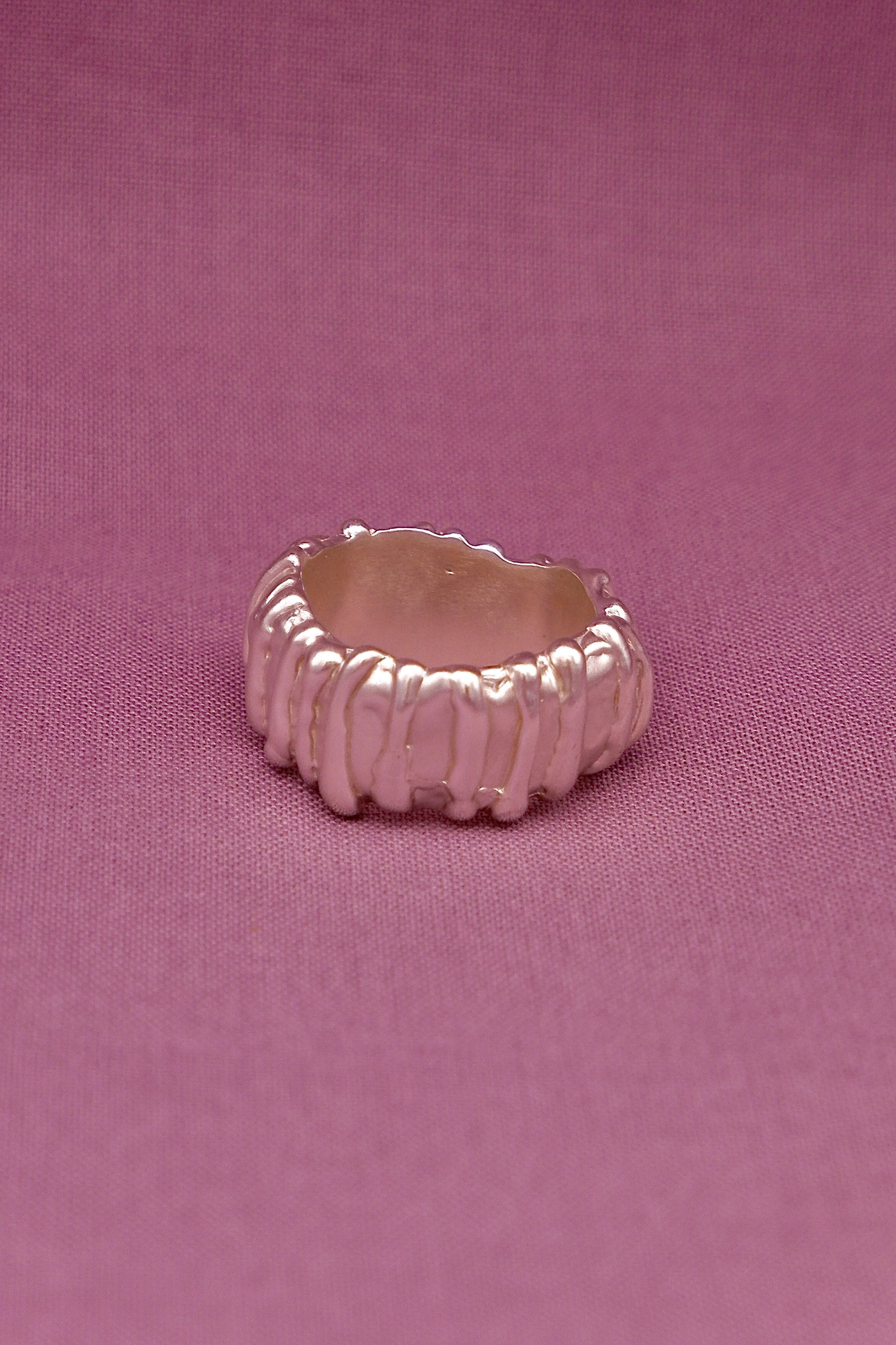 Silver ring with textured design on a pink background