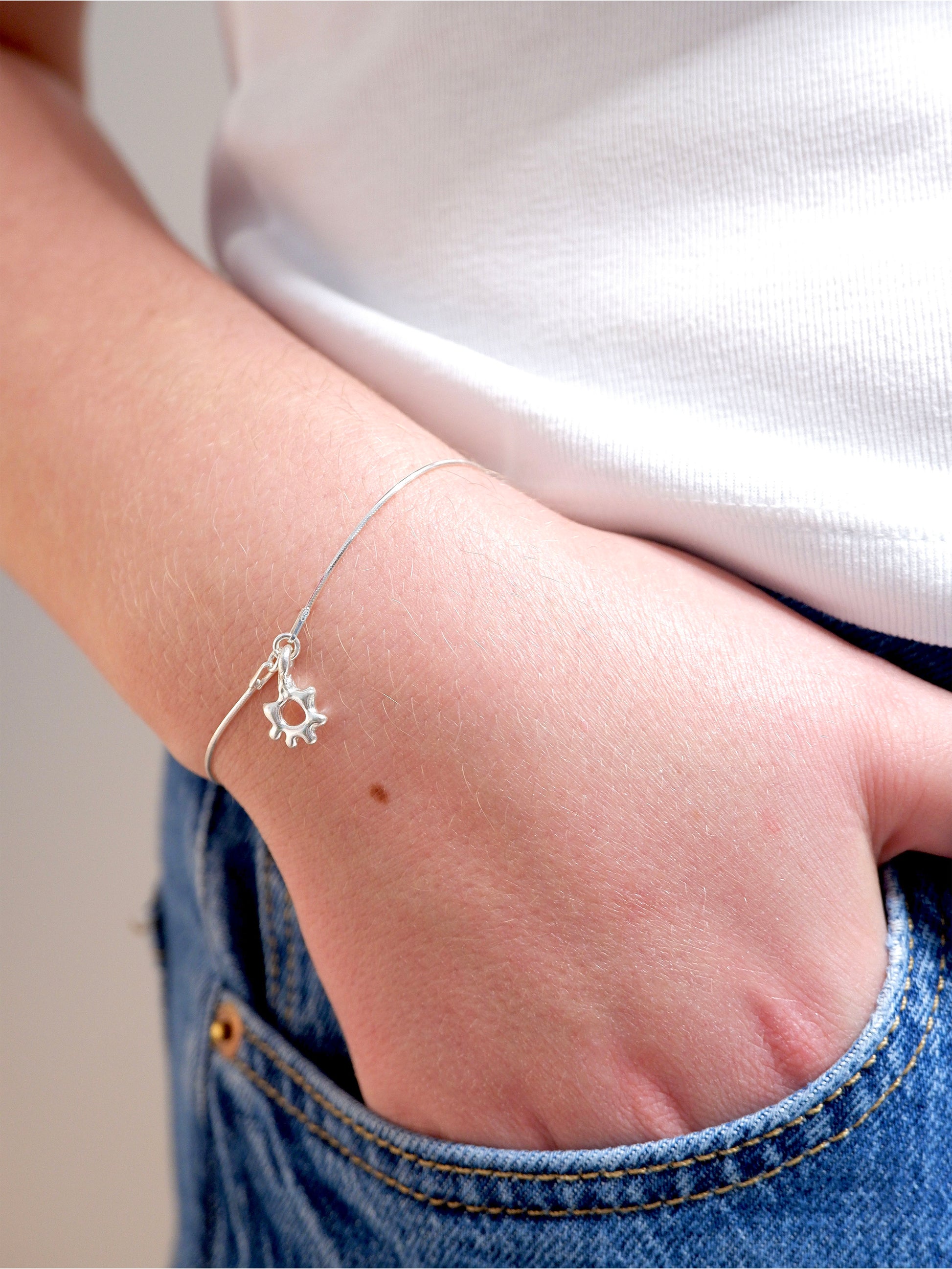 Silver bracelet with a small decorative element on a wrist, wearing a white shirt and blue jeans.