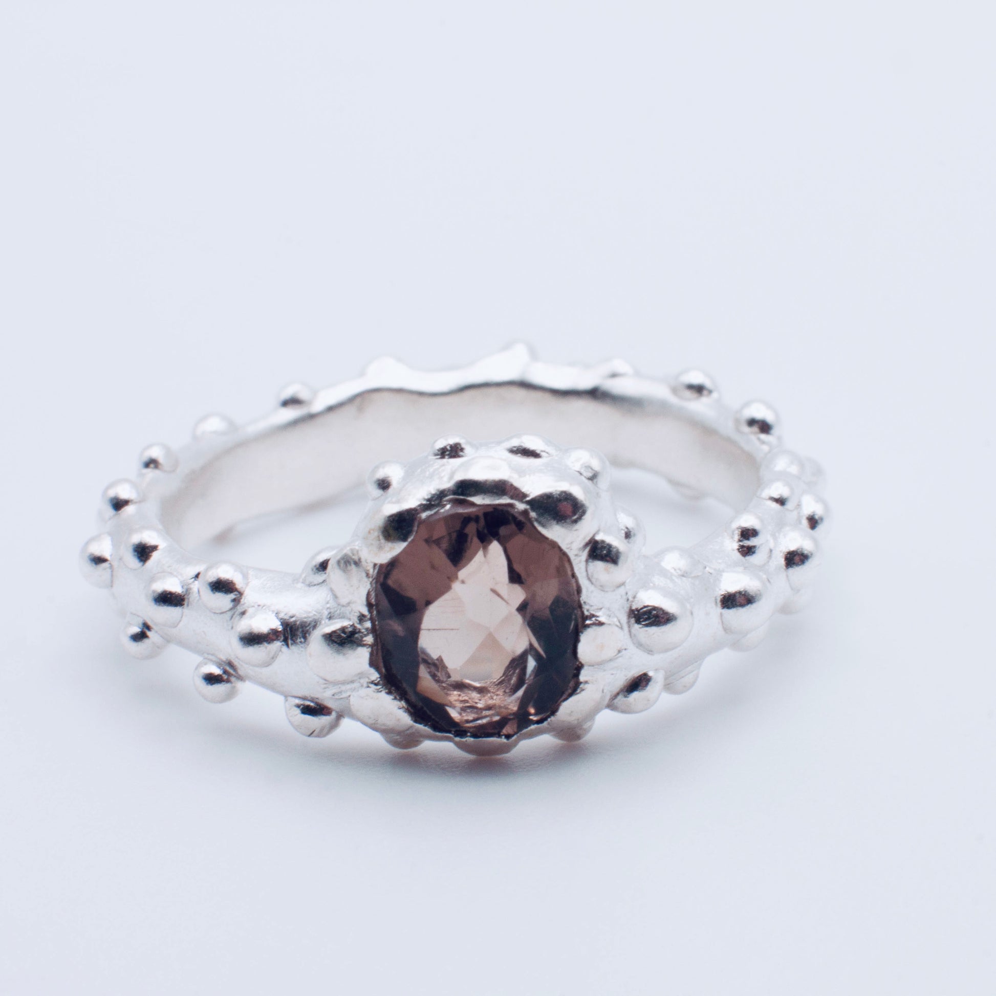 Silver ring with a central gemstone on a light gray background