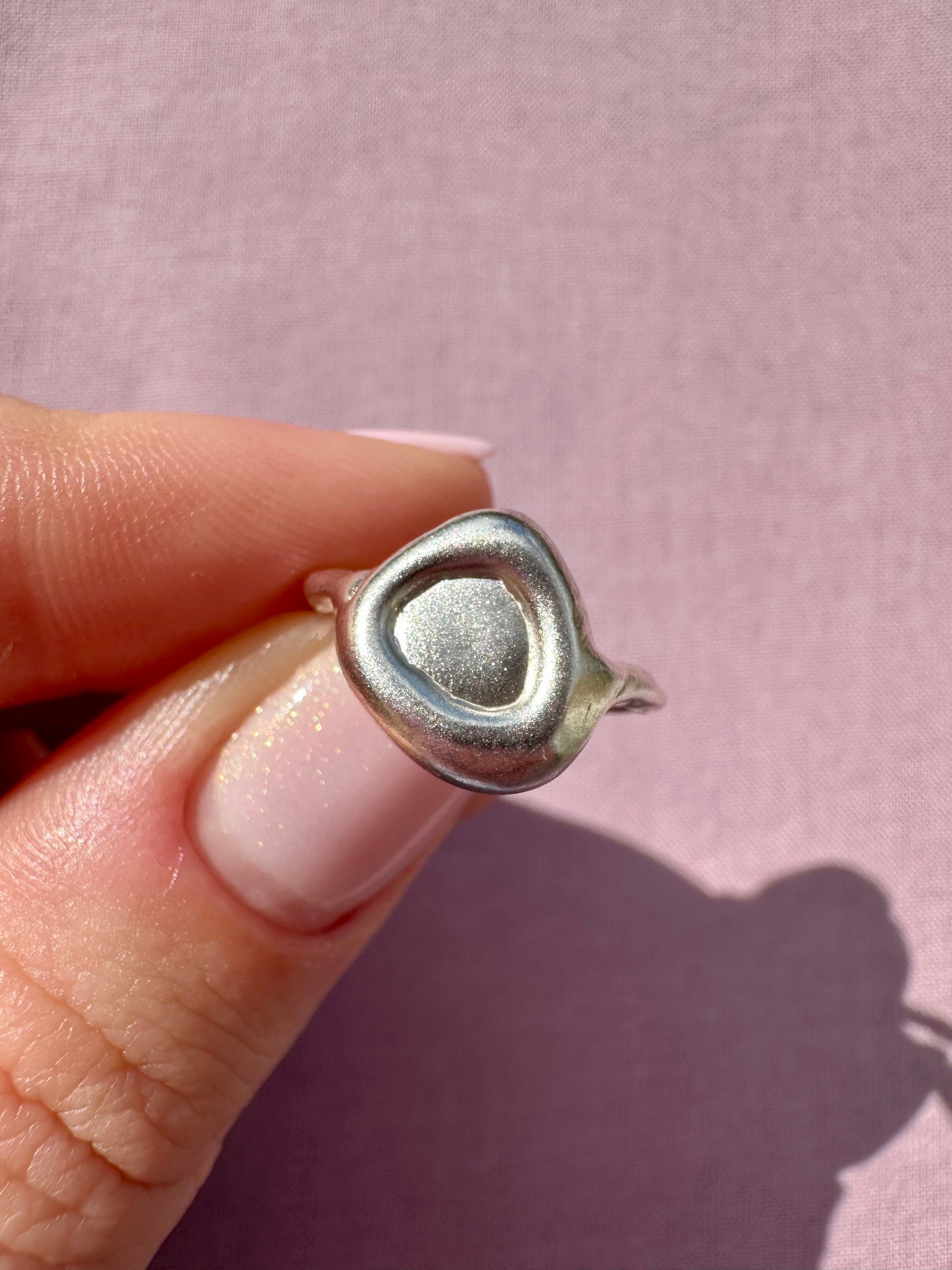 Silver  ring held between fingers against a pink background