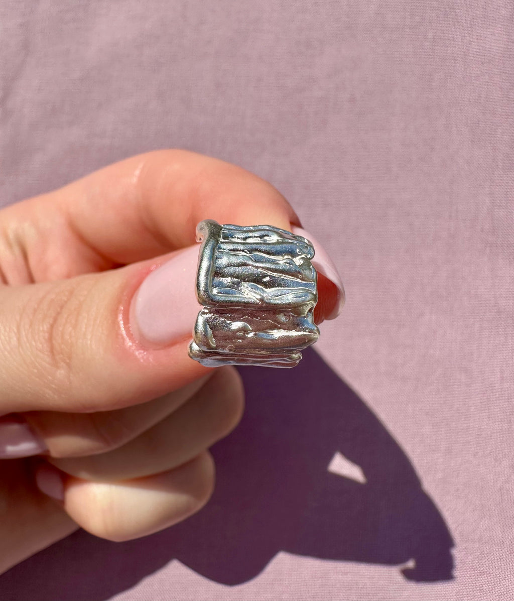 Silver earring held in a hand against a pink background