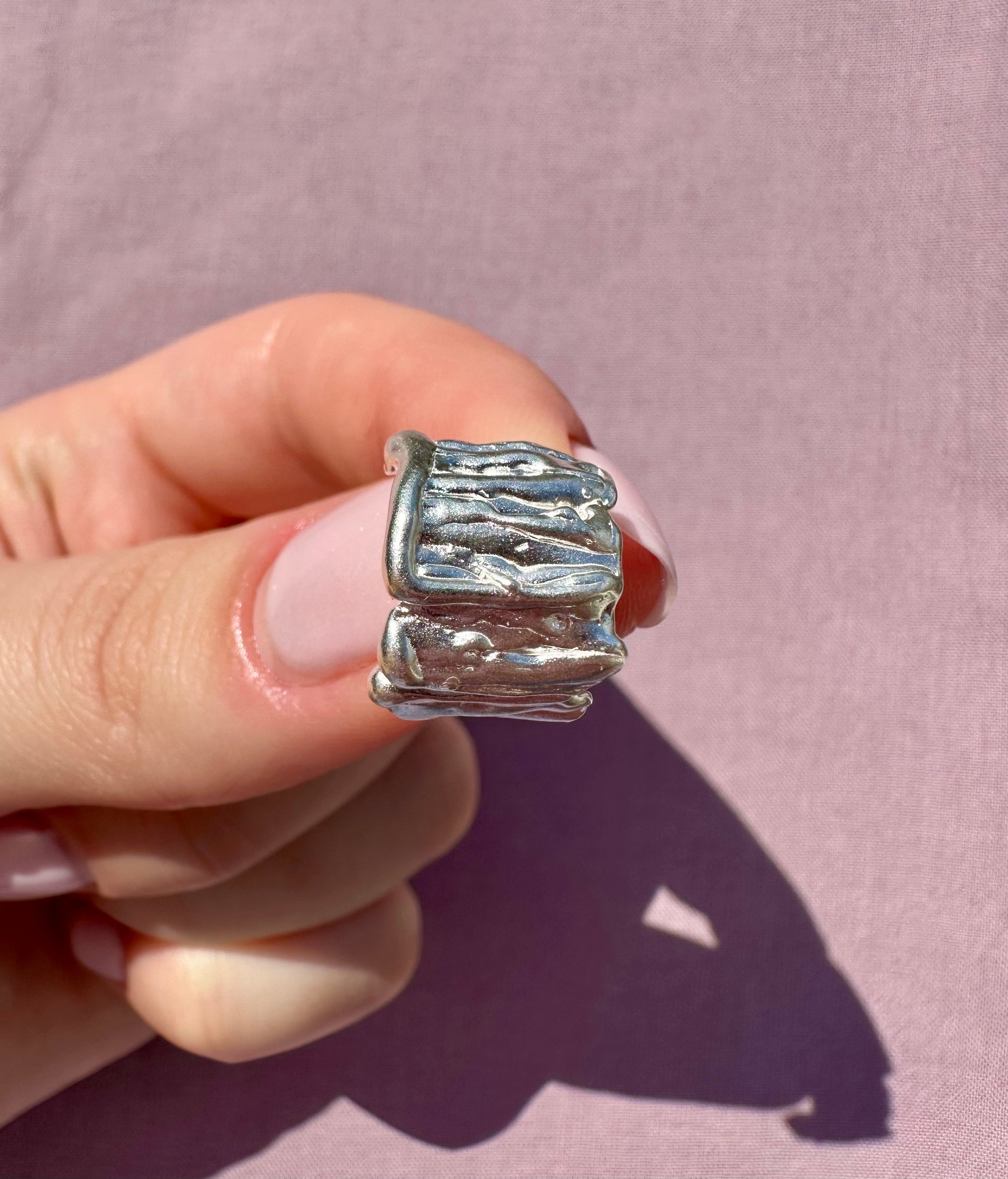 Silver earring held in a hand against a pink background