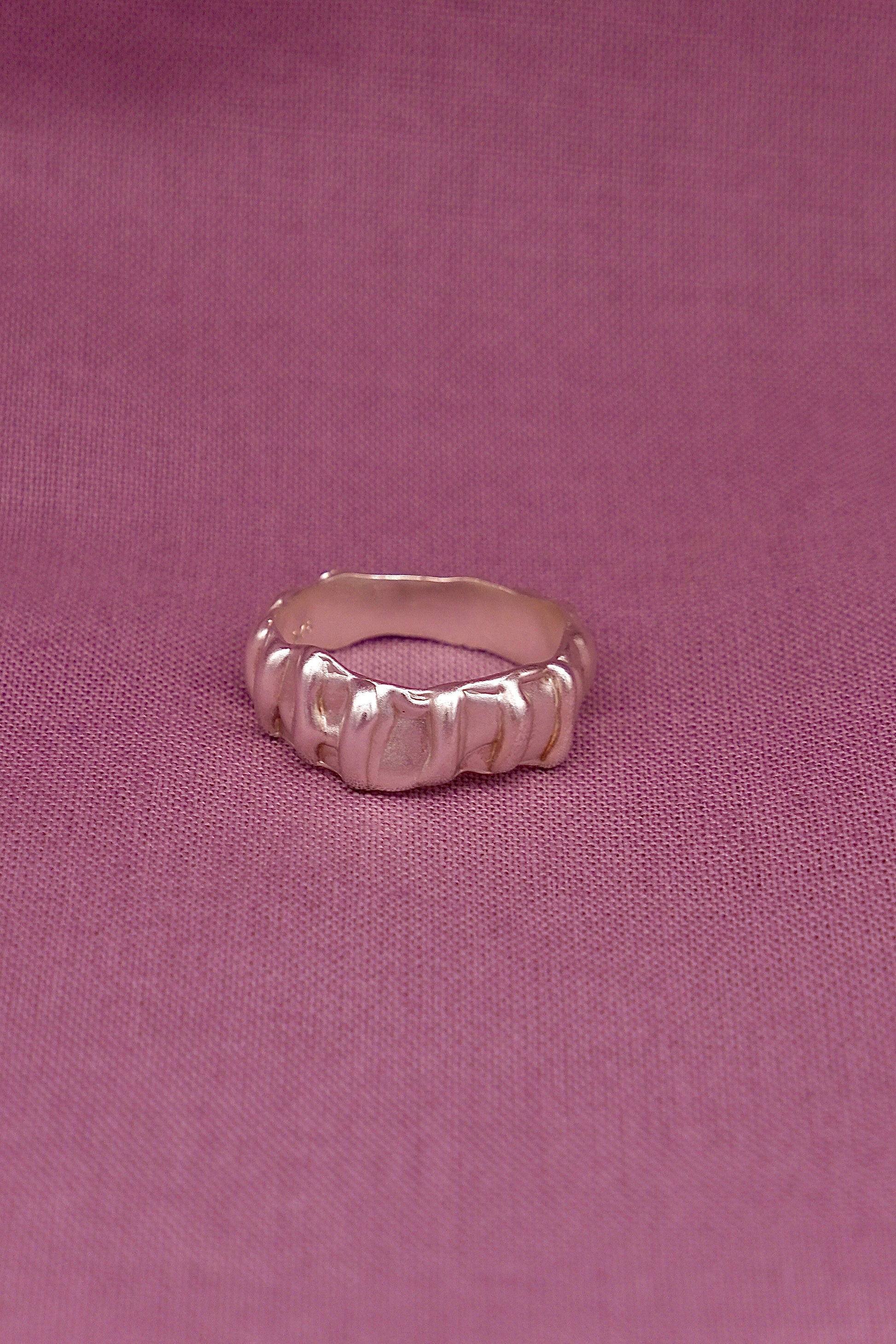 Silver ring with a textured design on a pink fabric background