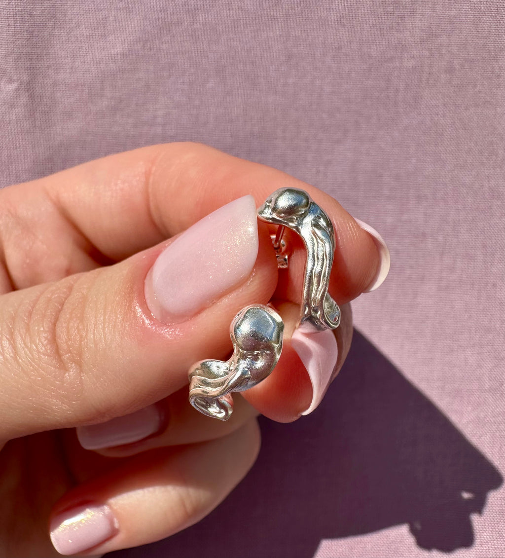 Silver ear cuff with gemstones held between fingers against a pink background