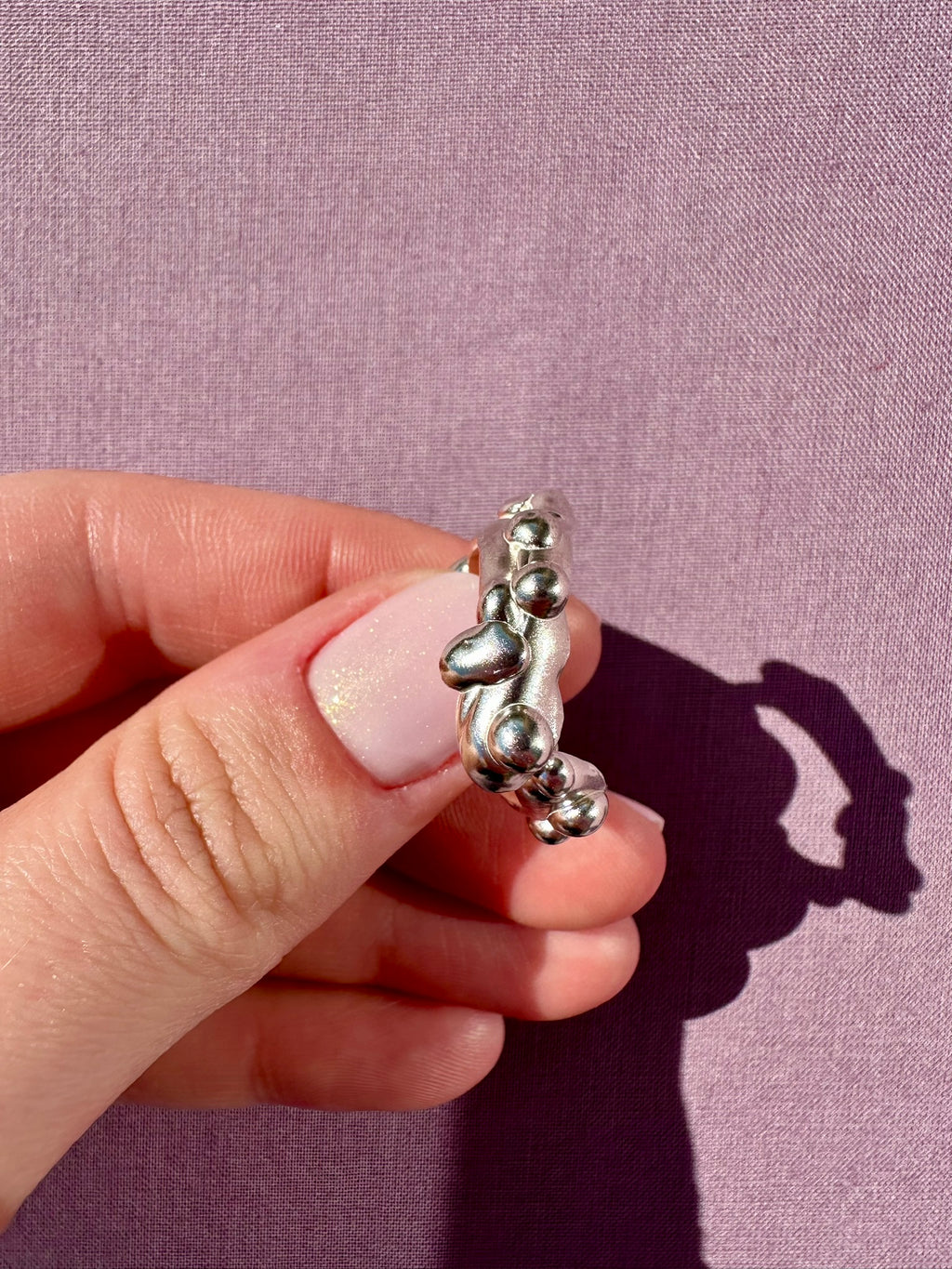 Silver ring held by a hand against a purple background
