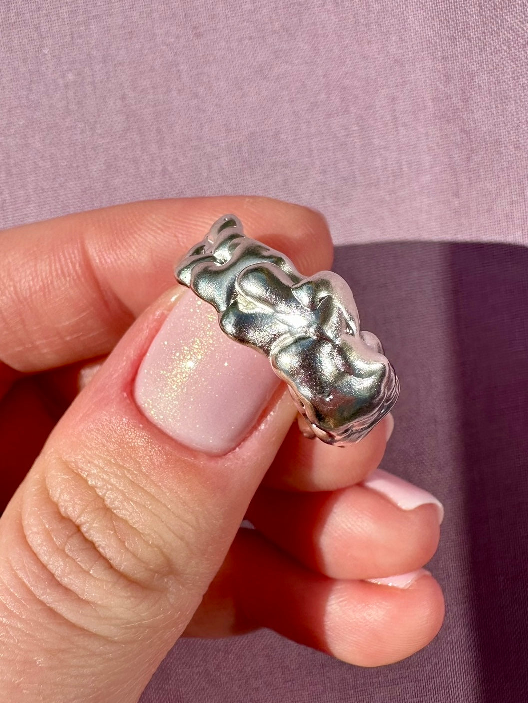 Silver ring held by a hand with a pink background