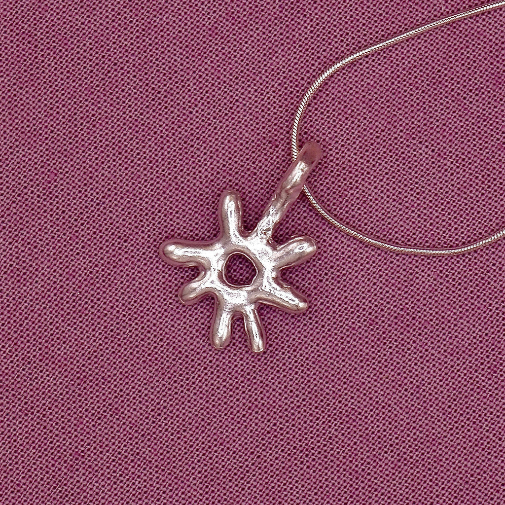 Silver sun-shaped pendant on a pink fabric background