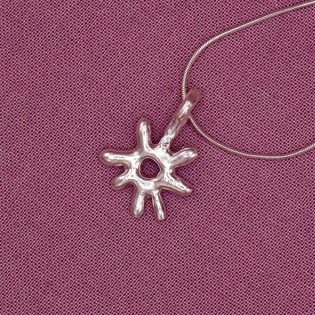 Silver sun-shaped pendant on a pink fabric background