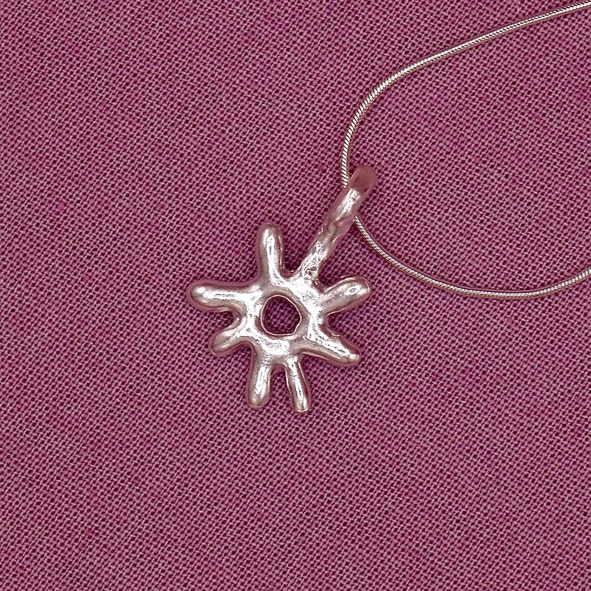 Silver sun-shaped pendant on a pink fabric background