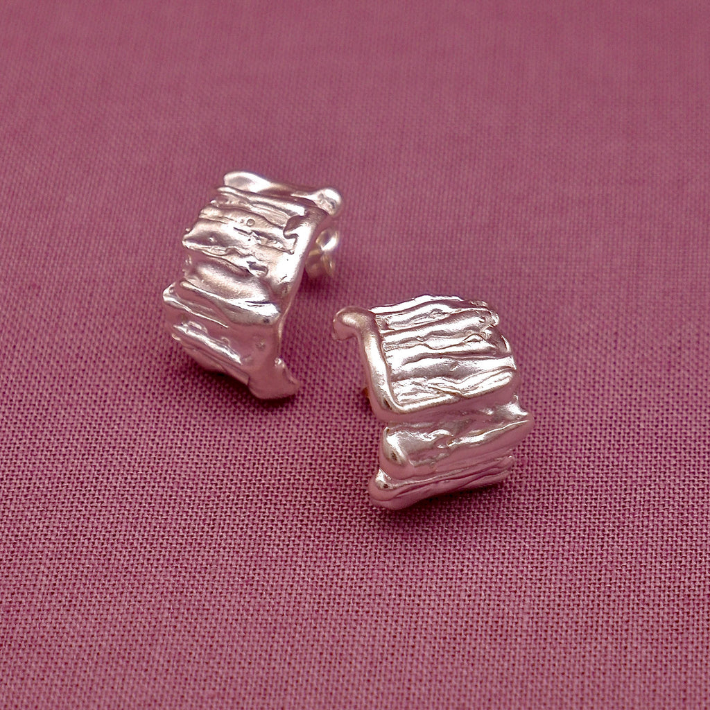 Silver textured square stud earrings on a pink fabric background
