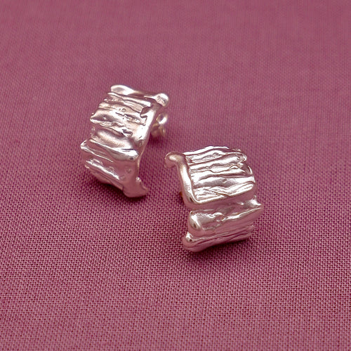 Silver textured square stud earrings on a pink fabric background