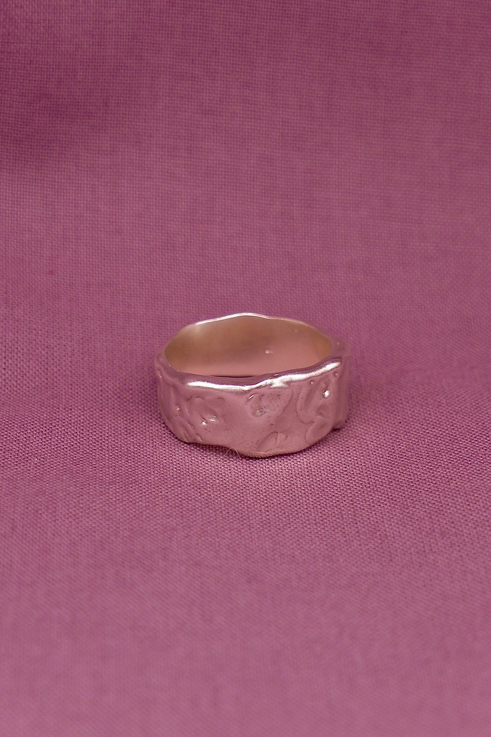 Silver ring with textured design on a pink fabric background
