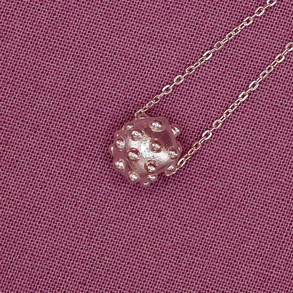 Silver necklace with a textured pendant on a pink fabric background