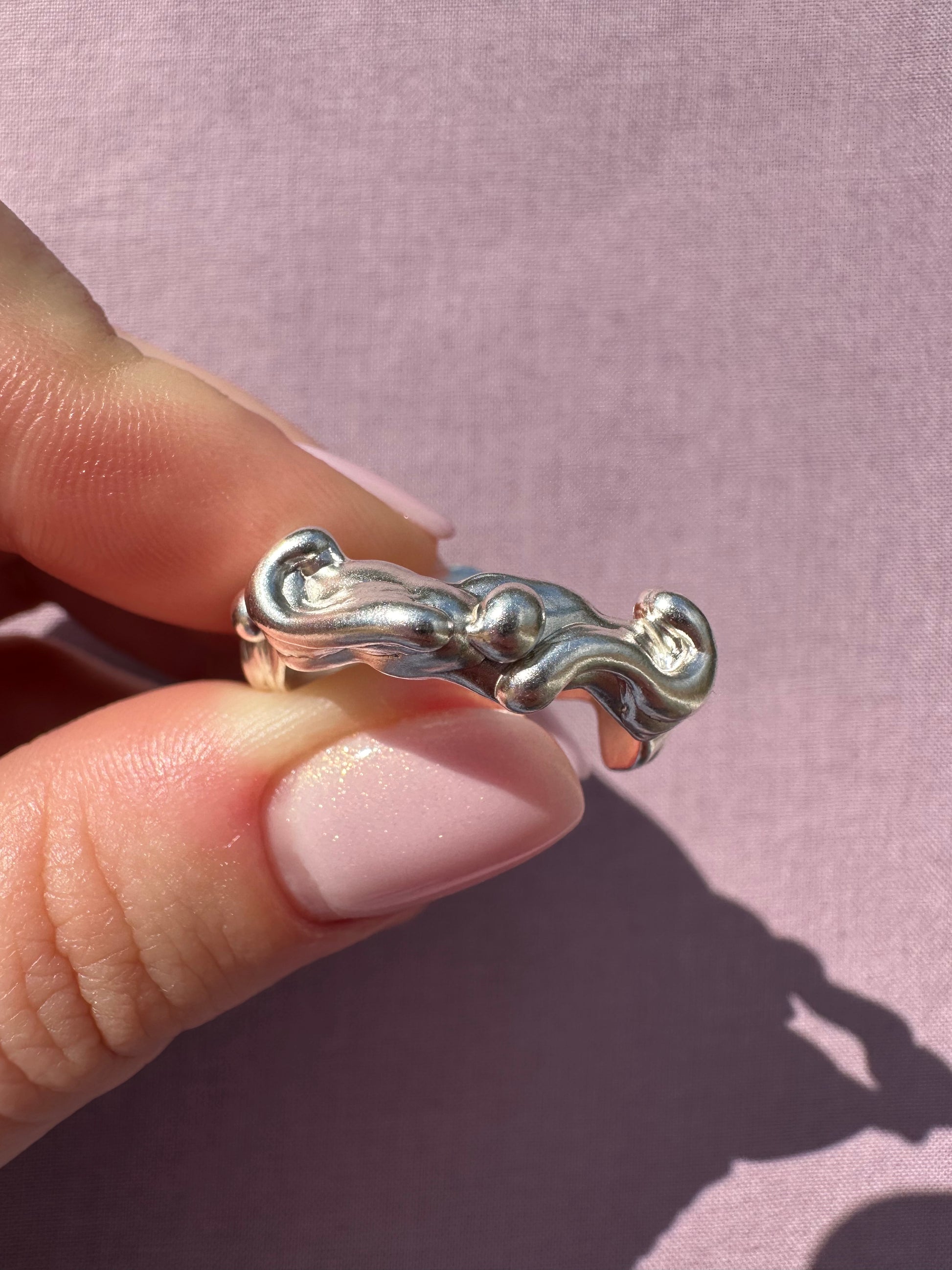 Silver ring held between fingers against a pink background
