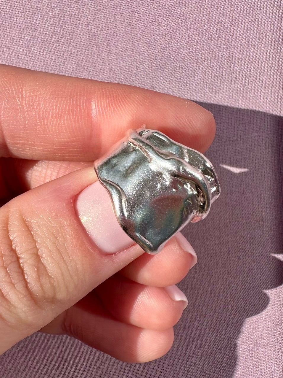 Silver ring held between fingers against a pink background