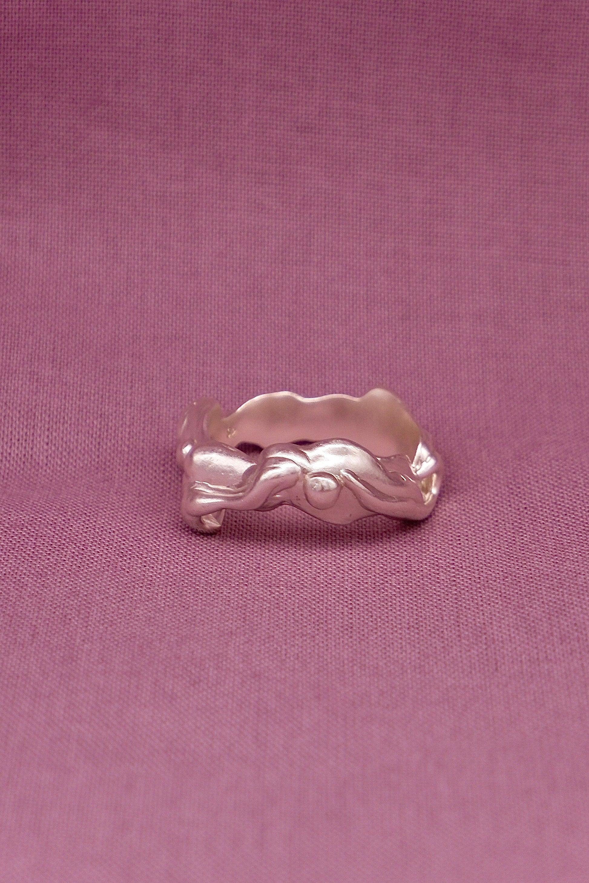 Silver ring with a wavy design on a pink fabric background
