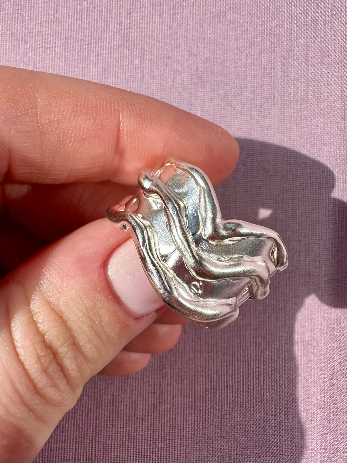 Silver ring held by a hand against a pink background
