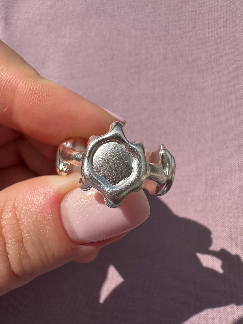 Silver ring held between fingers against a pink background