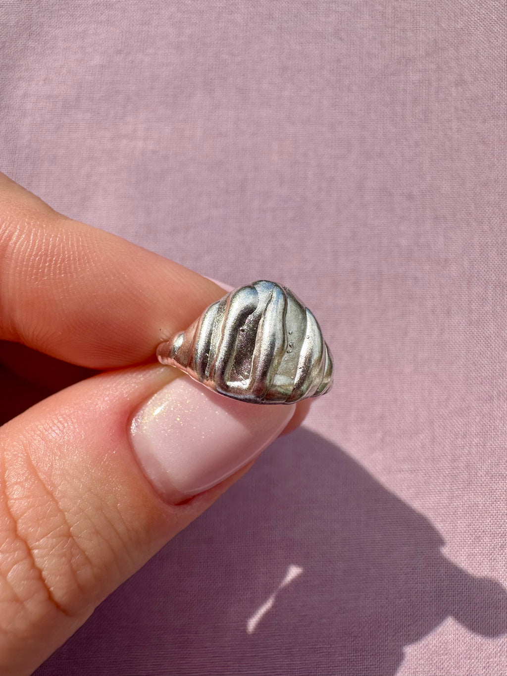 Silver ring held by a hand against a pink background