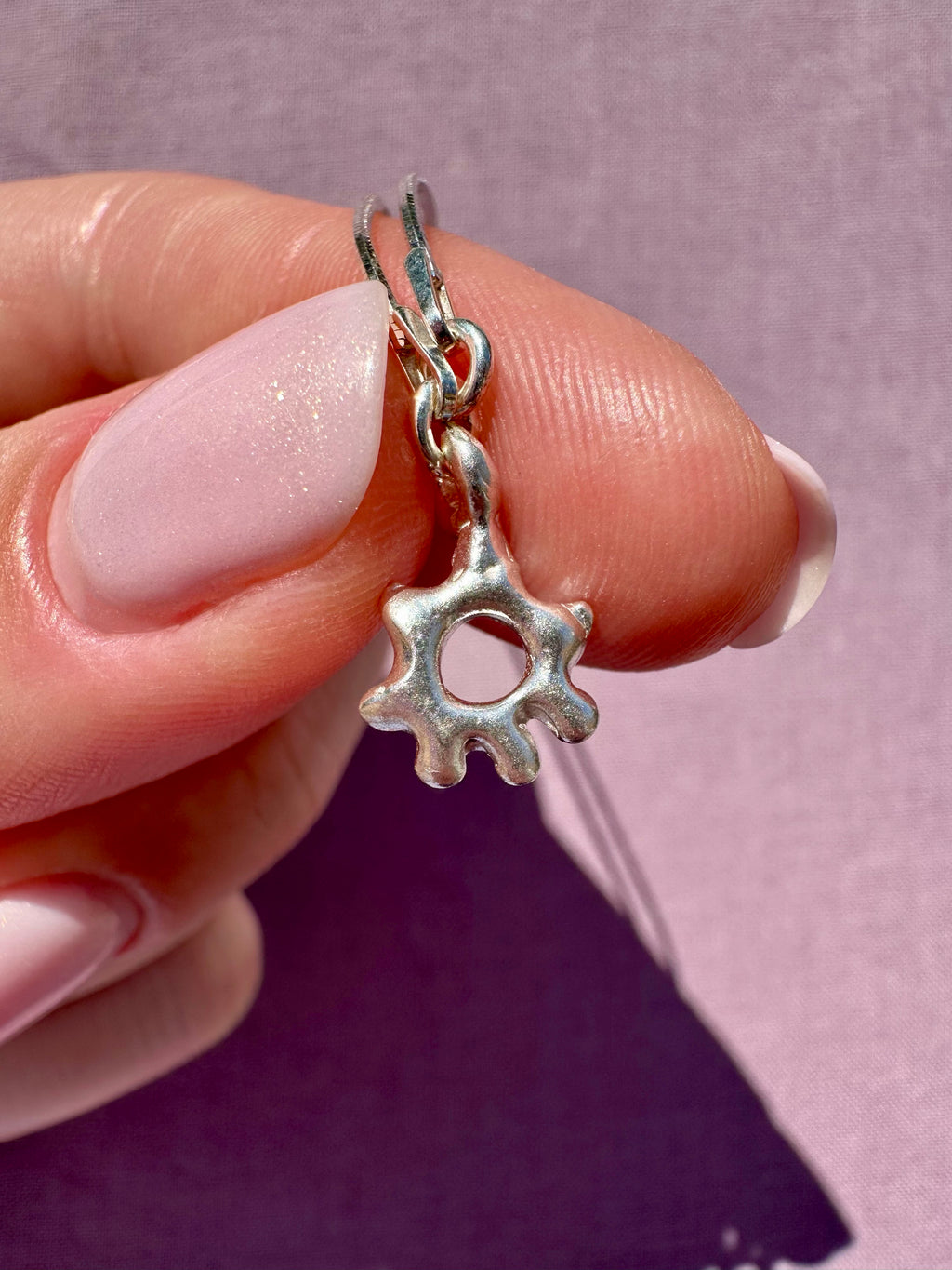 Silver charm shaped like a gear held between fingers against a pink background