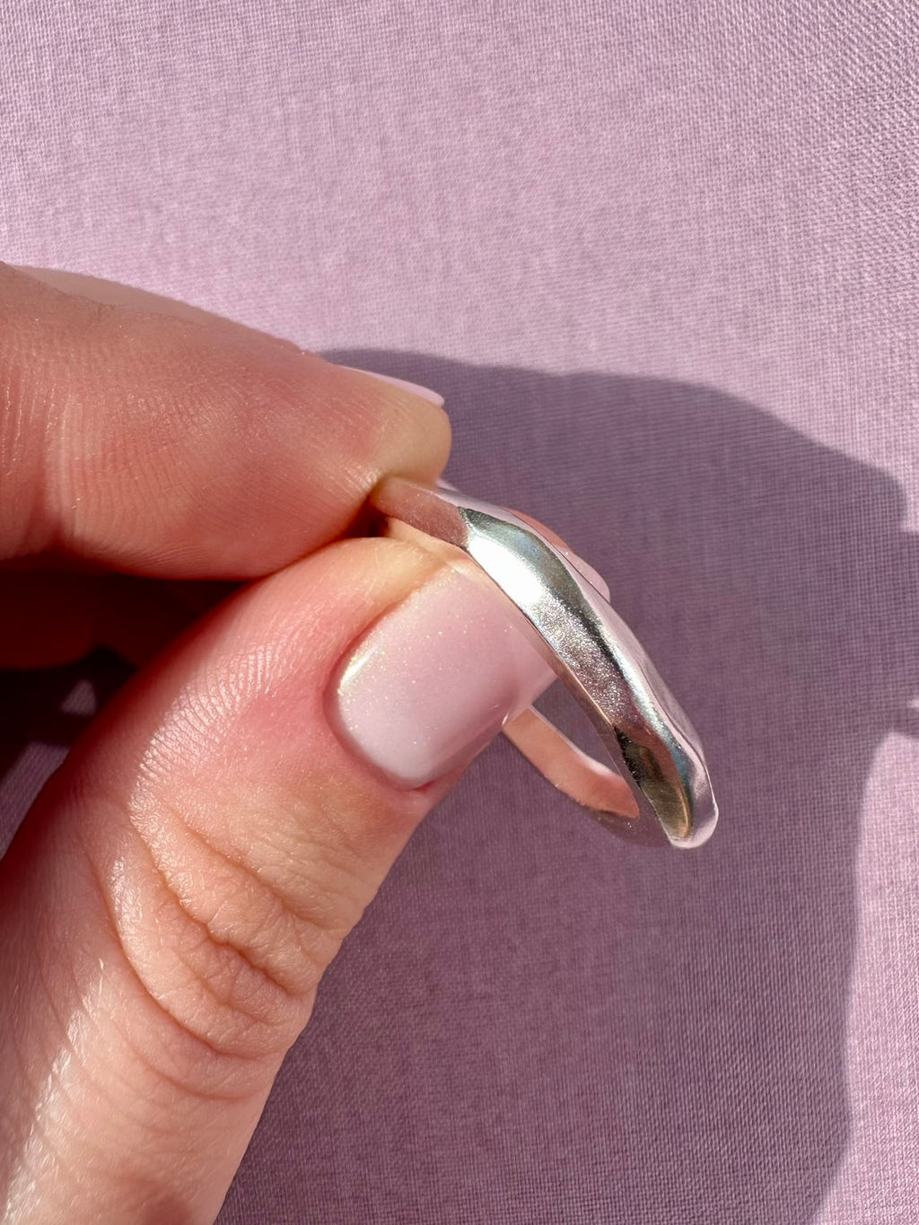 Hand holding a silver ring against a pink background