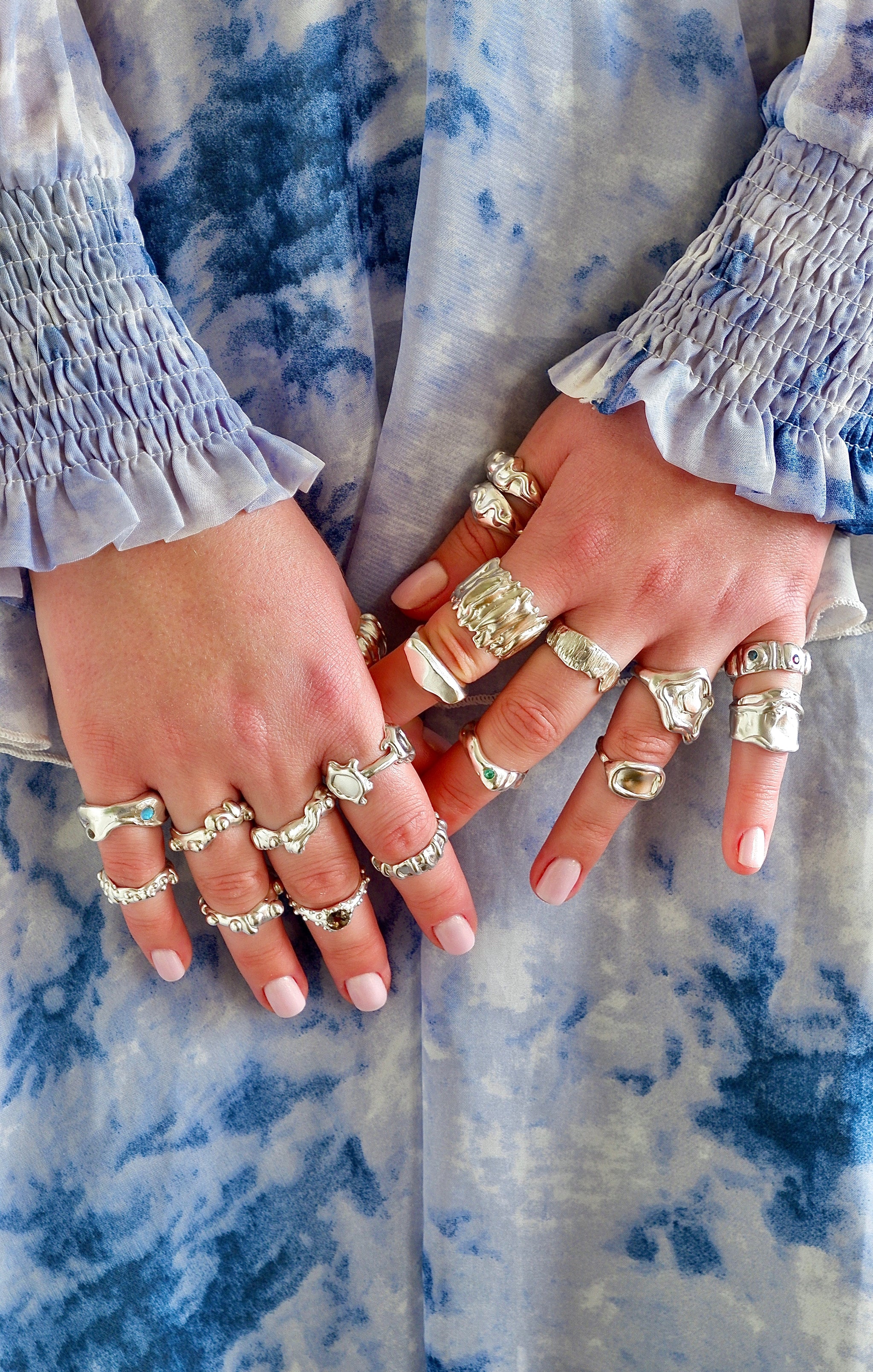 Close-up of hands with multiple rings on a blue and white patterned fabric background