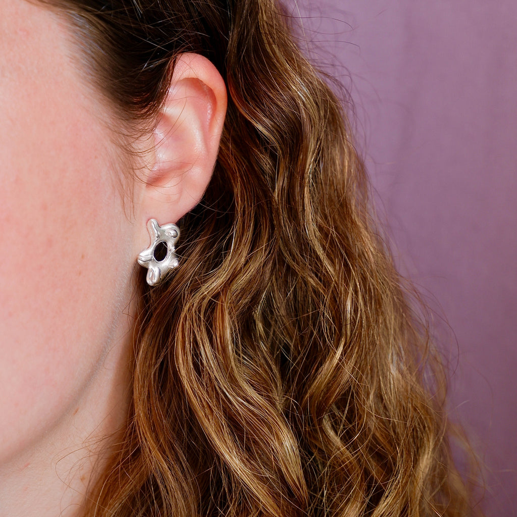 Close-up of a person wearing a silver flower-shaped earring with a purple background