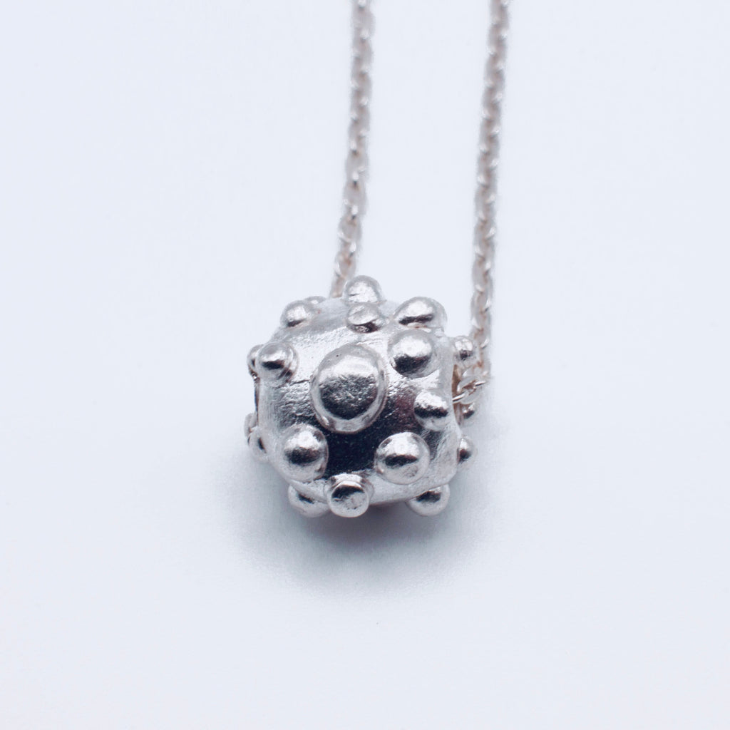Silver textured sphere pendant on a chain against a white background