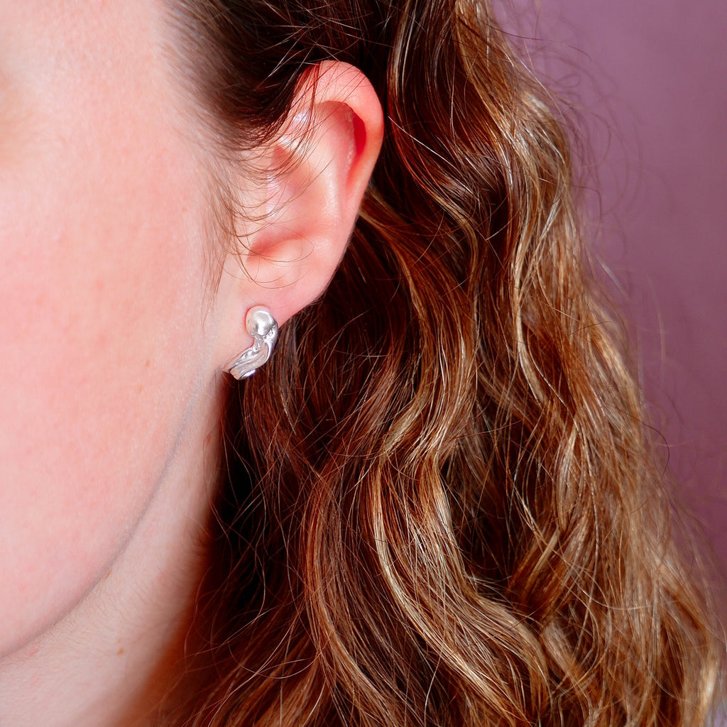 Close-up of an ear wearing a silver earring with wavy design, hair partially covering face.