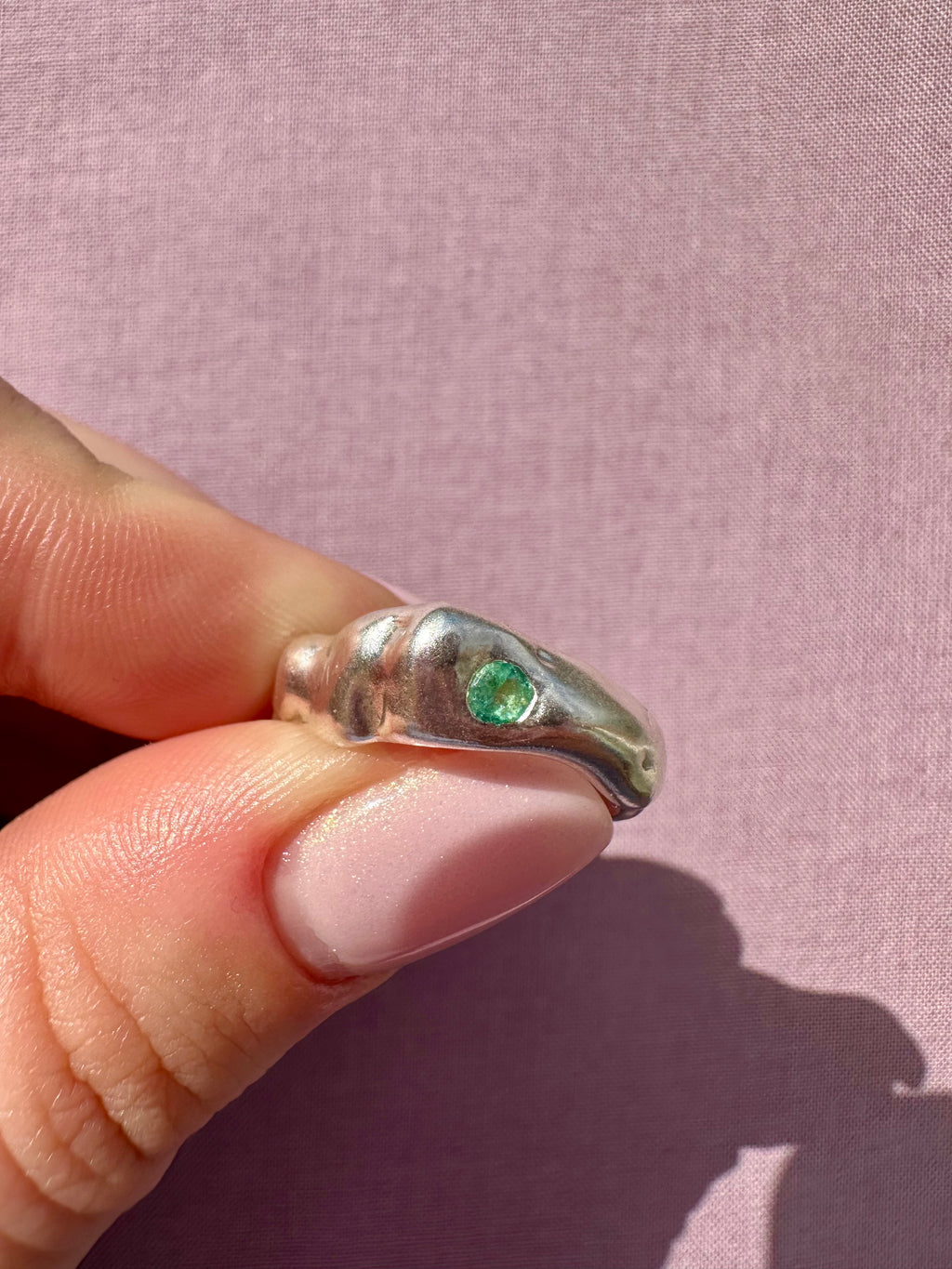Silver ring with a green gemstone on a pink fabric background
