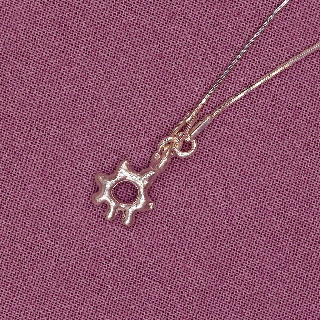 Silver sun-shaped pendant on a chain against a purple fabric background