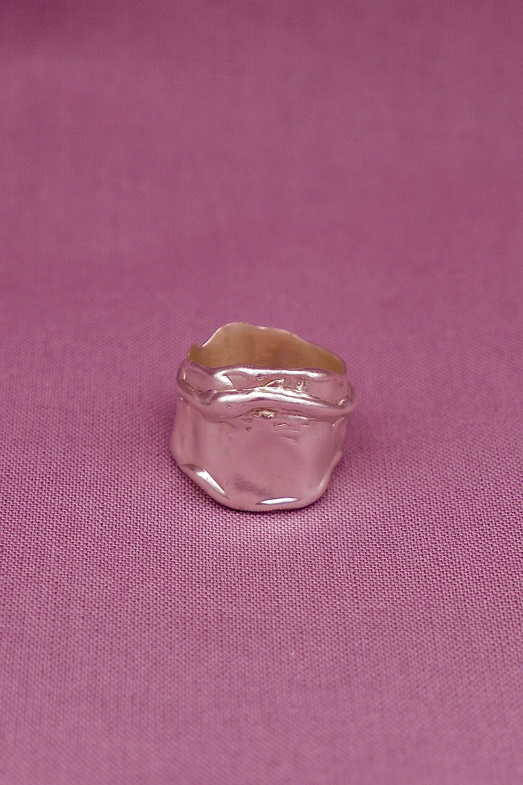 Silver ring with a gold band on a pink fabric background