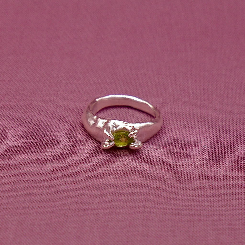 Silver ring with a green gemstone on a pink fabric background